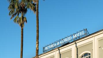 A building with a sign reading "Victoria & Alfred Hotel" and tall palm trees in front.