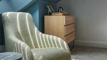Una habitación con techo inclinado, un sillón verde a rayas, un aparador de madera y una mesa redonda.