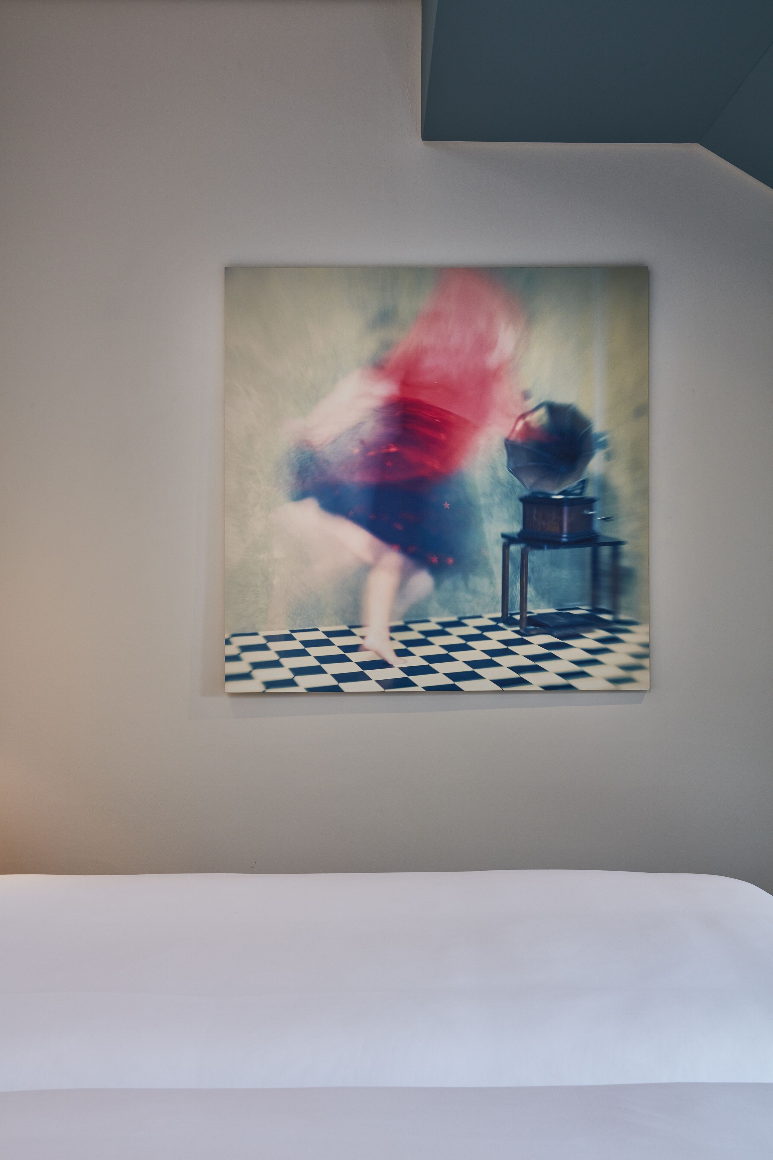 Una pintura que muestra a una persona con un vestido rojo sobre un piso de cuadros y una pequeña mesa.