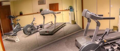 A gym with stationary bikes, a treadmill, and a mirrored wall.