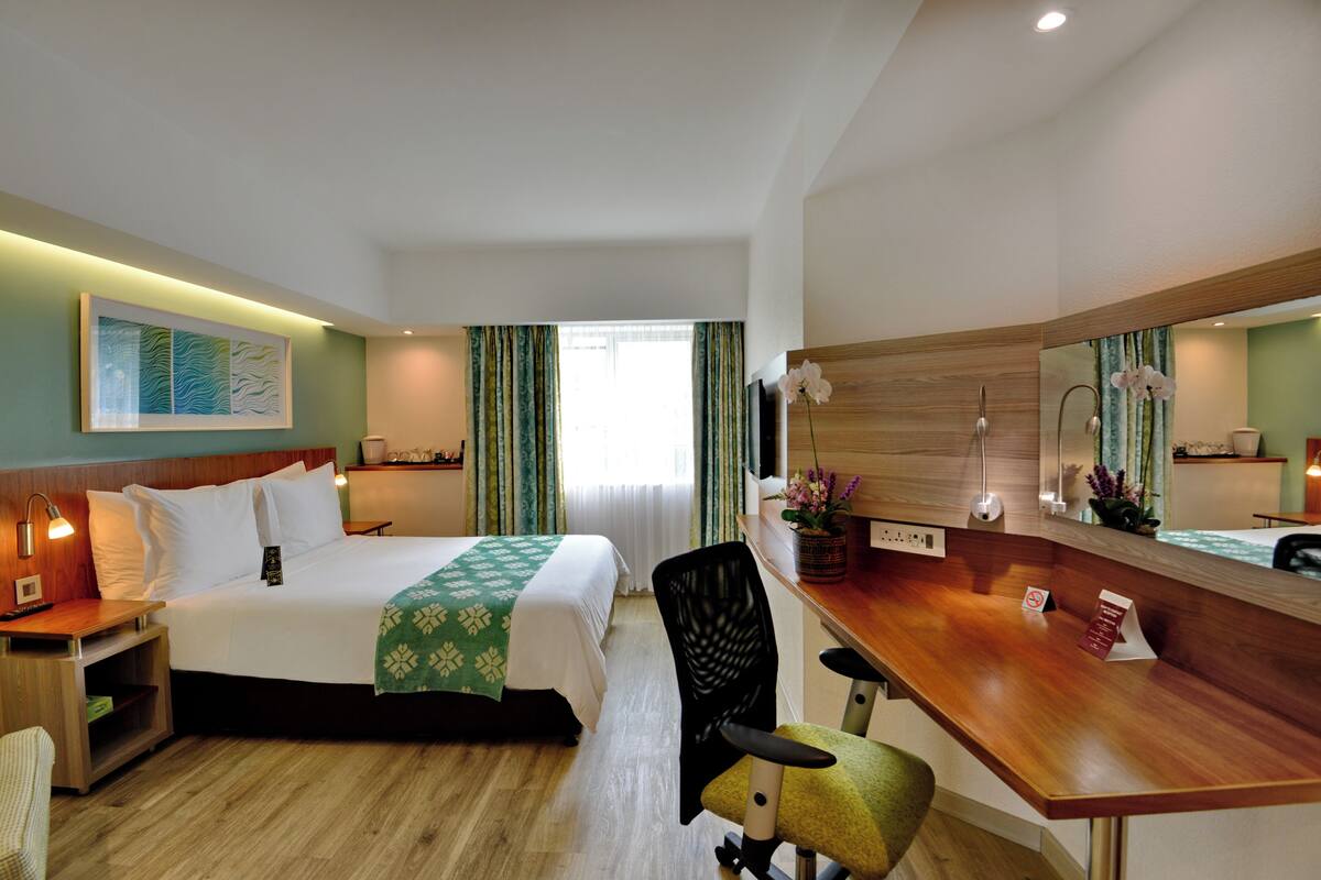 A hotel room with a bed, desk, chair, and a large mirror.