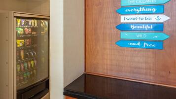 A vending machine with various snacks and drinks, and a wooden wall with a sign that reads "The ocean is everything I want to be Beautiful Wild and free."