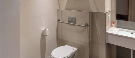 Un baño moderno con inodoro, barra de apoyo, contenedor de basura y perchero para toallas.