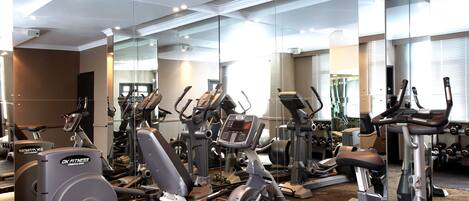 A gym with various exercise machines, a mirrored wall, and a large window.
