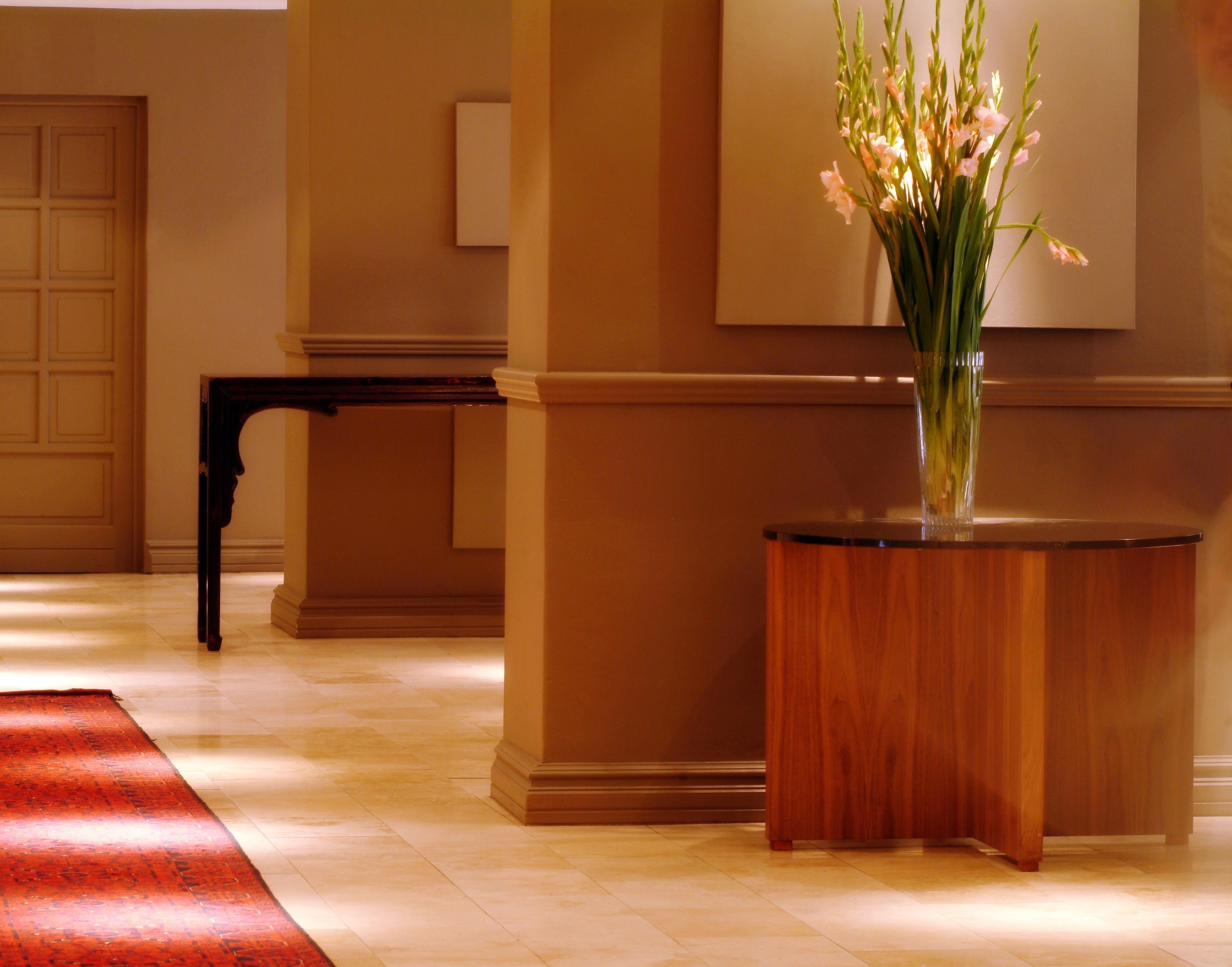 Un hall d’entrée avec un comptoir de réception en bois, un vase rempli de fleurs et un tapis rouge.