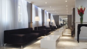 Un moderno vestíbulo de hotel con sofás negros, mesas blancas y lámparas.