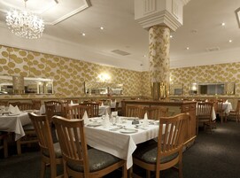 Un comedor formal con sillas y mesas de madera, una araña y un papel tapiz estampado.
