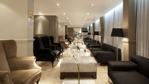 Un vestíbulo de hotel con una larga recepción, varias zonas de estar con sofás y sillones, y un letrero que indica la ubicación de los baños.