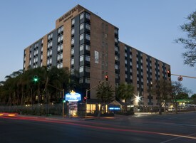 Un hotel de varios pisos con fachada de ladrillo, múltiples balcones y un llamativo letrero que dice "Manhattan Hotel" en la parte superior.