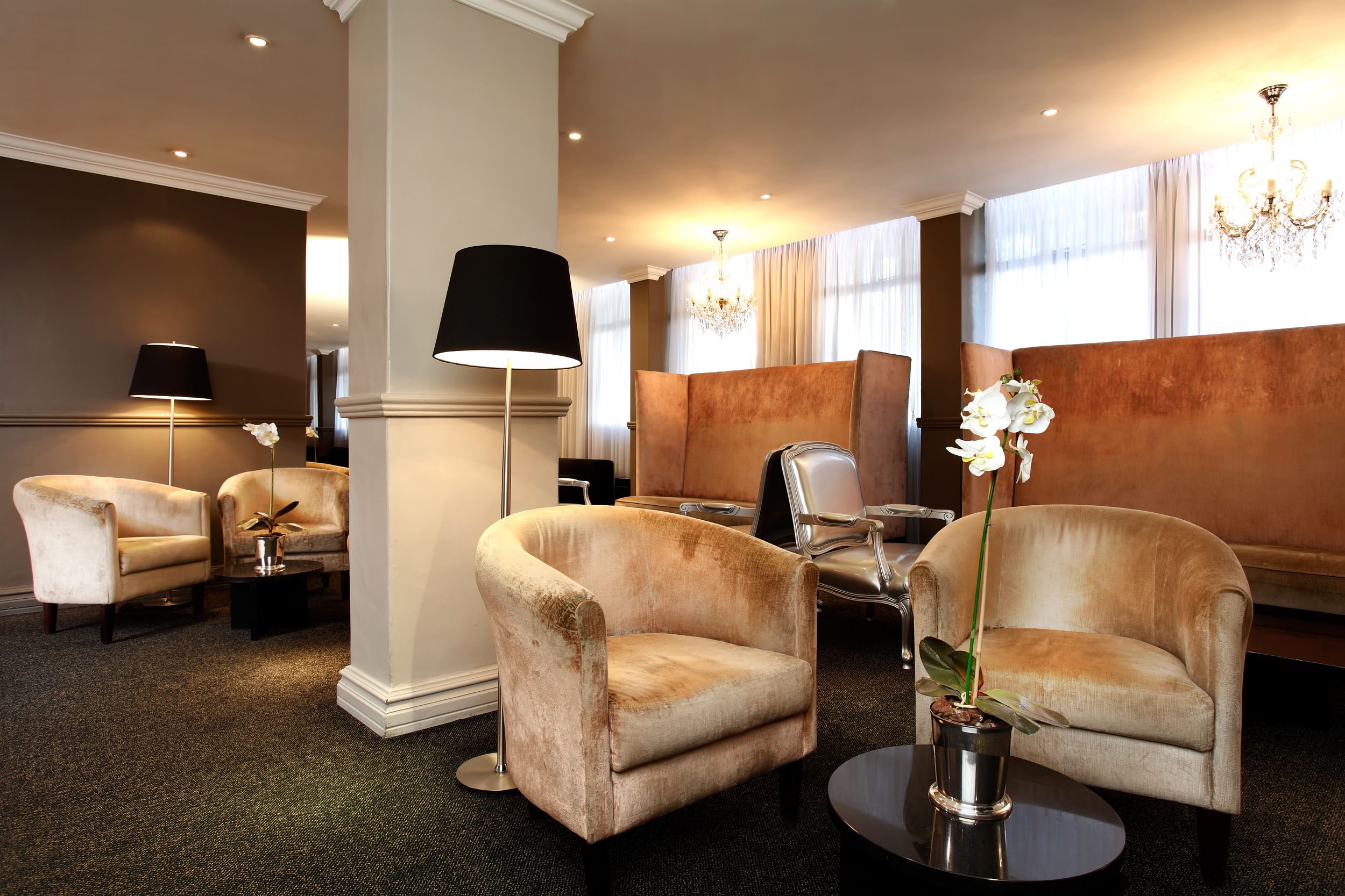 A hotel lobby with plush armchairs, a floor lamp, and a chandelier.