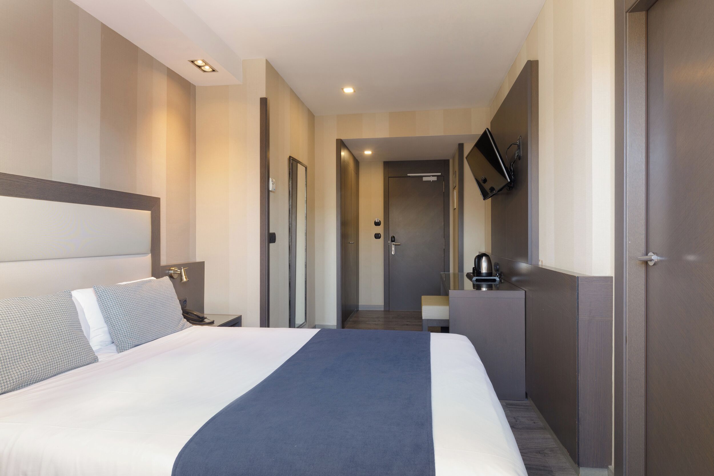 Une chambre d’hôtel avec un grand lit, un bureau, une chaise, un téléviseur fixé au mur et une porte donnant sur une salle de bain.