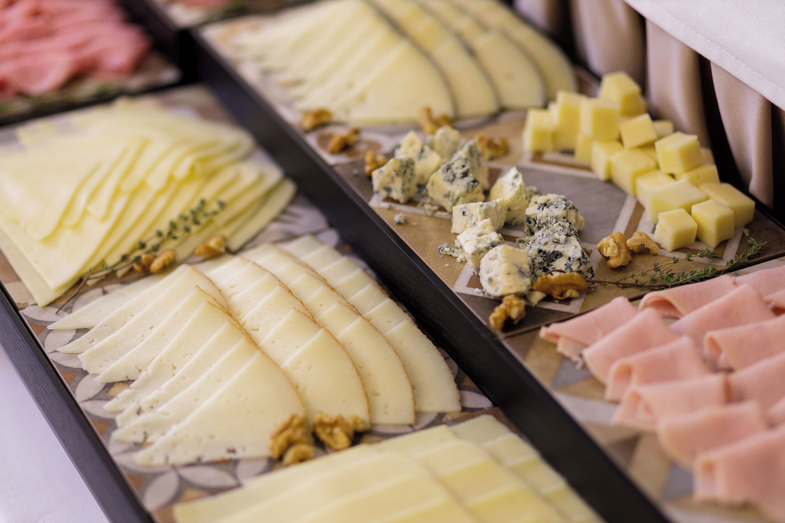 Un plateau de fromages comprenant différents types de fromages, notamment du fromage bleu et du cheddar, ainsi que des noix et du jambon en tranches.
