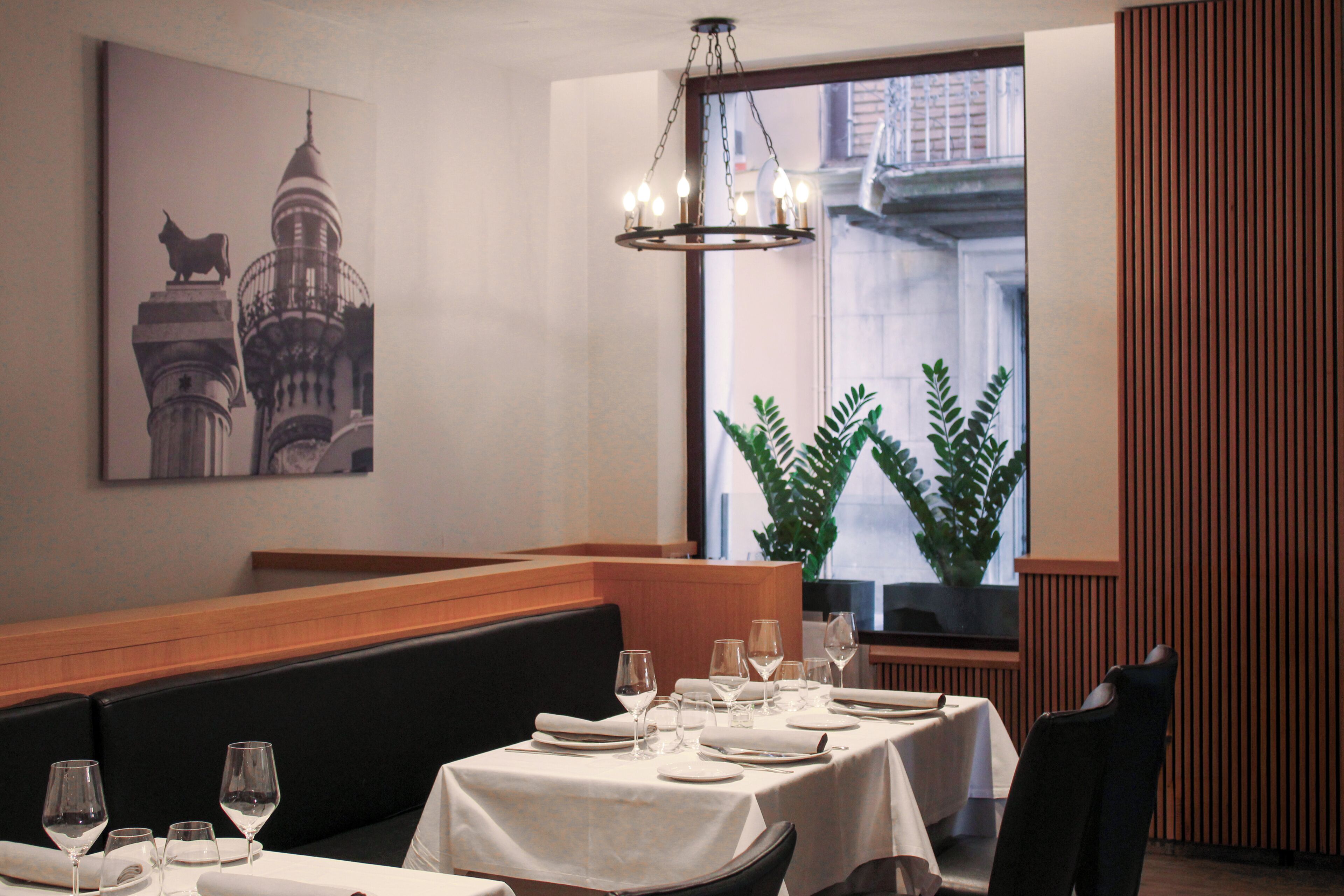A dining area with a table set for a meal, a chandelier, a large window with a view, and a wall-mounted artwork.