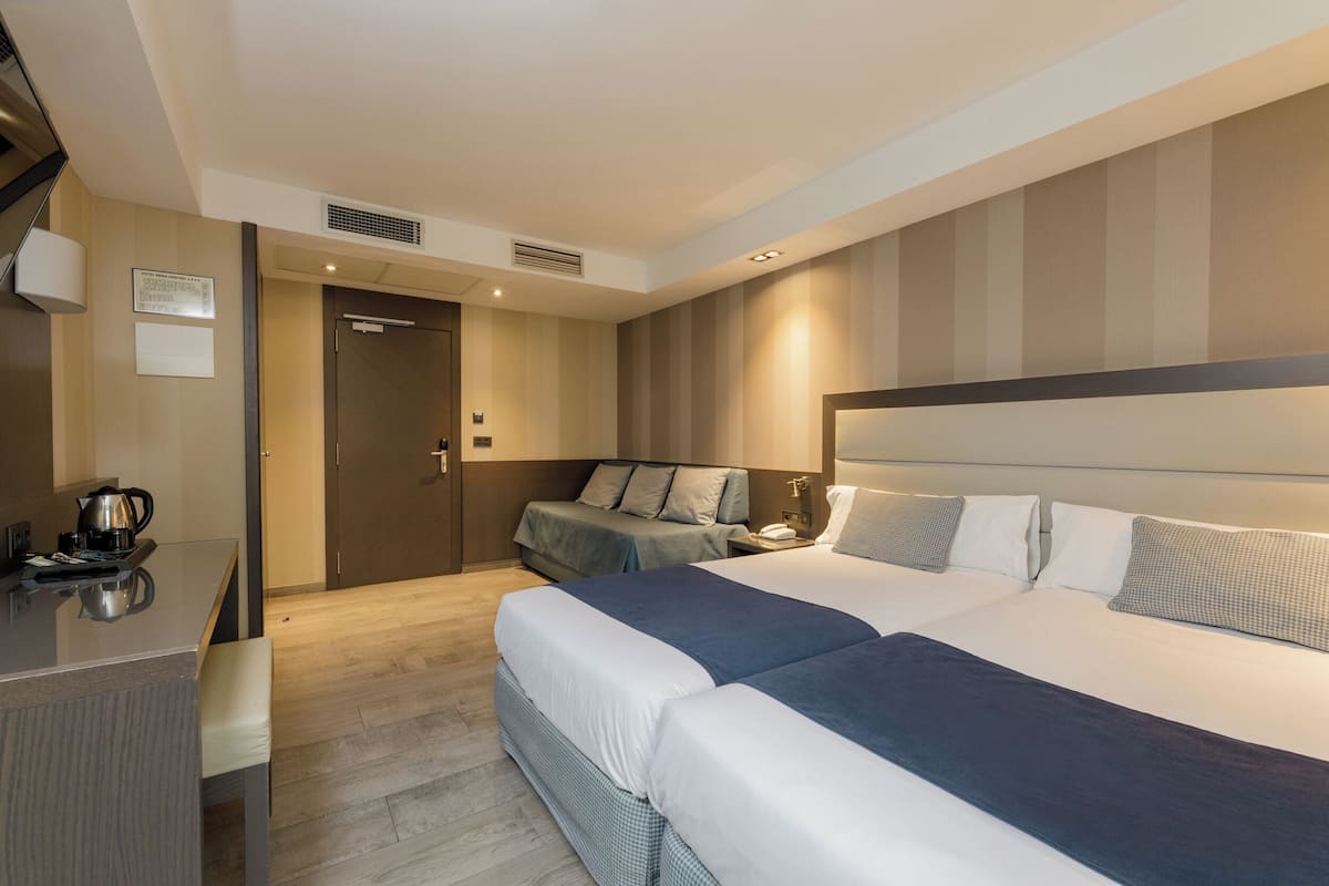 Una habitación de hotel moderna con una cama grande, un escritorio con un hervidor y una zona de estar separada con un sofá.