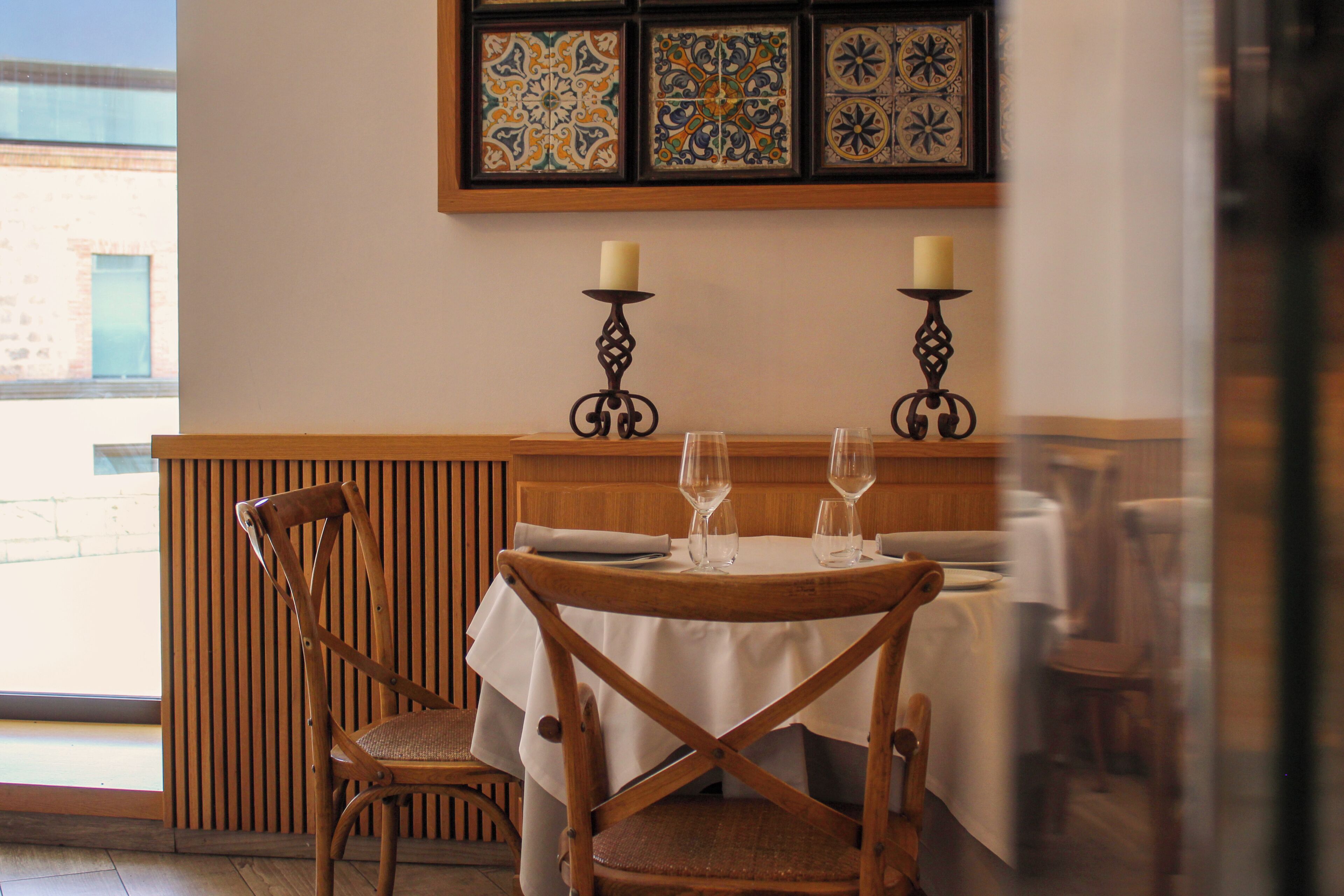 A dining area with a table set for two, two candles, and a chair.