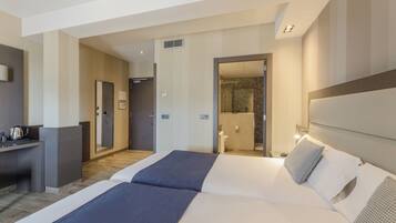 Habitación de hotel con una cama grande, un escritorio con hervidor y un baño visible a través de una puerta abierta.