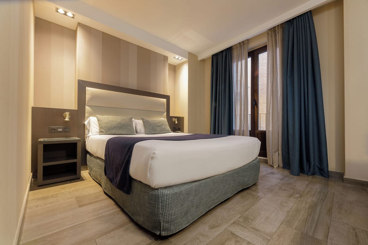 Una habitación de hotel moderna con una cama grande, una mesita de noche y una lámpara de noche.