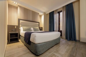 Hotellihuone, jossa on suuri sänky, yöpöydät, yölamppu ja ikkuna, jossa on verhot.