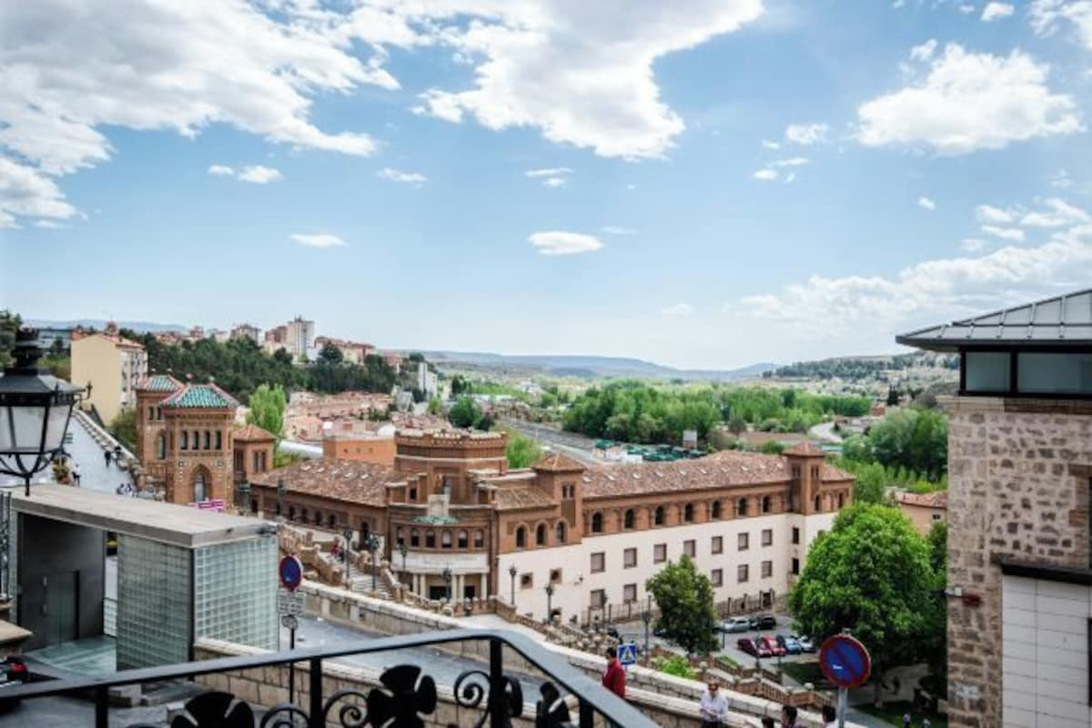 Un paisaje urbano con edificios históricos, cielo despejado y una vista distante de colinas.
