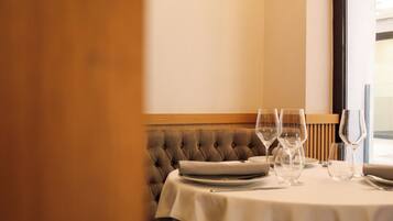 Una mesa de comedor con mantel blanco, un banco tapizado, copas y platos vacíos.
