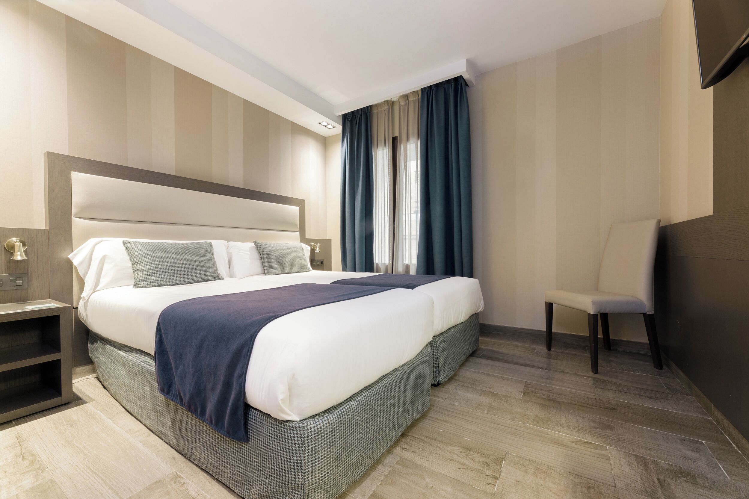 Una habitación de hotel moderna con una cama grande, una mesita de noche, una silla y un televisor montado en la pared.