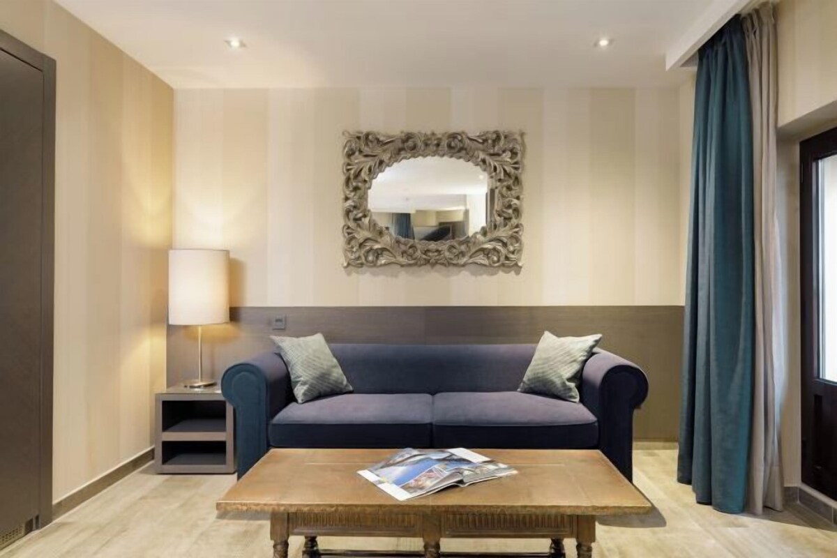 A modern hotel room with a dark blue sofa, a wooden coffee table, and a decorative mirror on the wall.