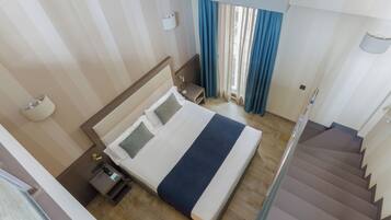 Una habitación de hotel con cama, mesita de noche, lámpara, ventana con cortinas y una escalera.