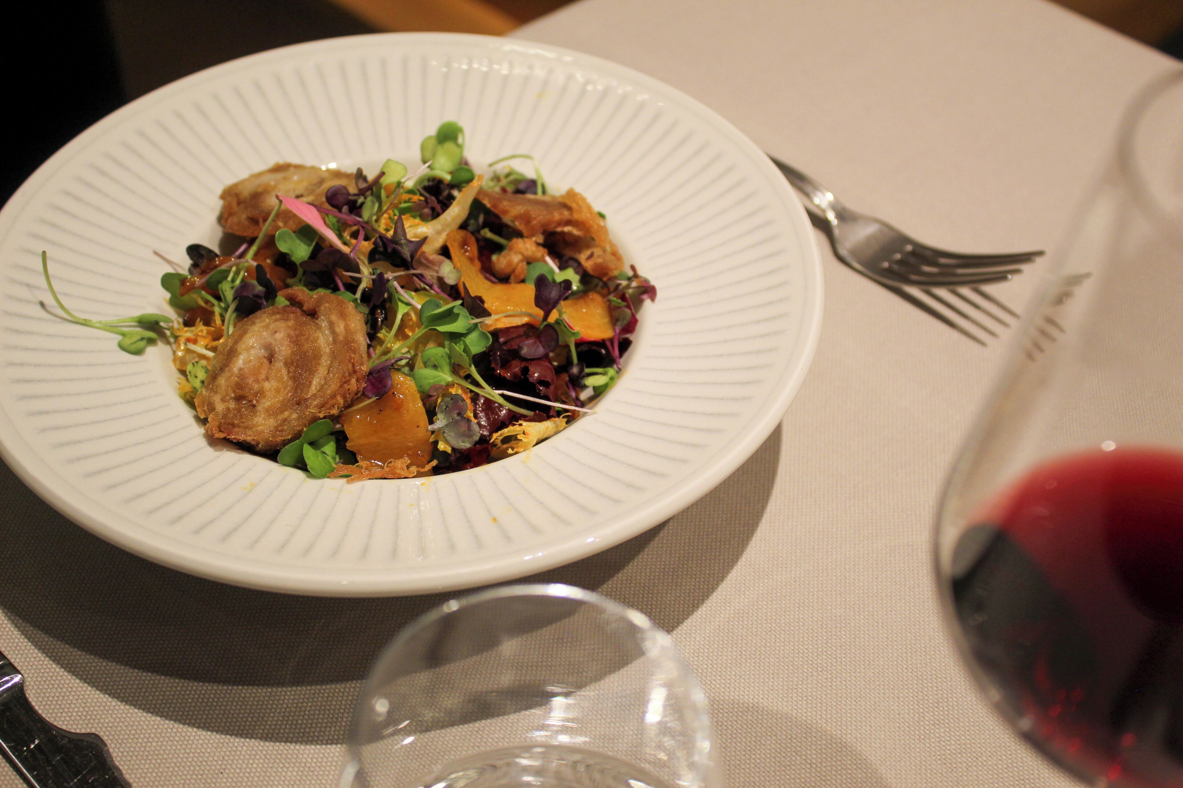 A white plate with food and a glass of red wine on a table.