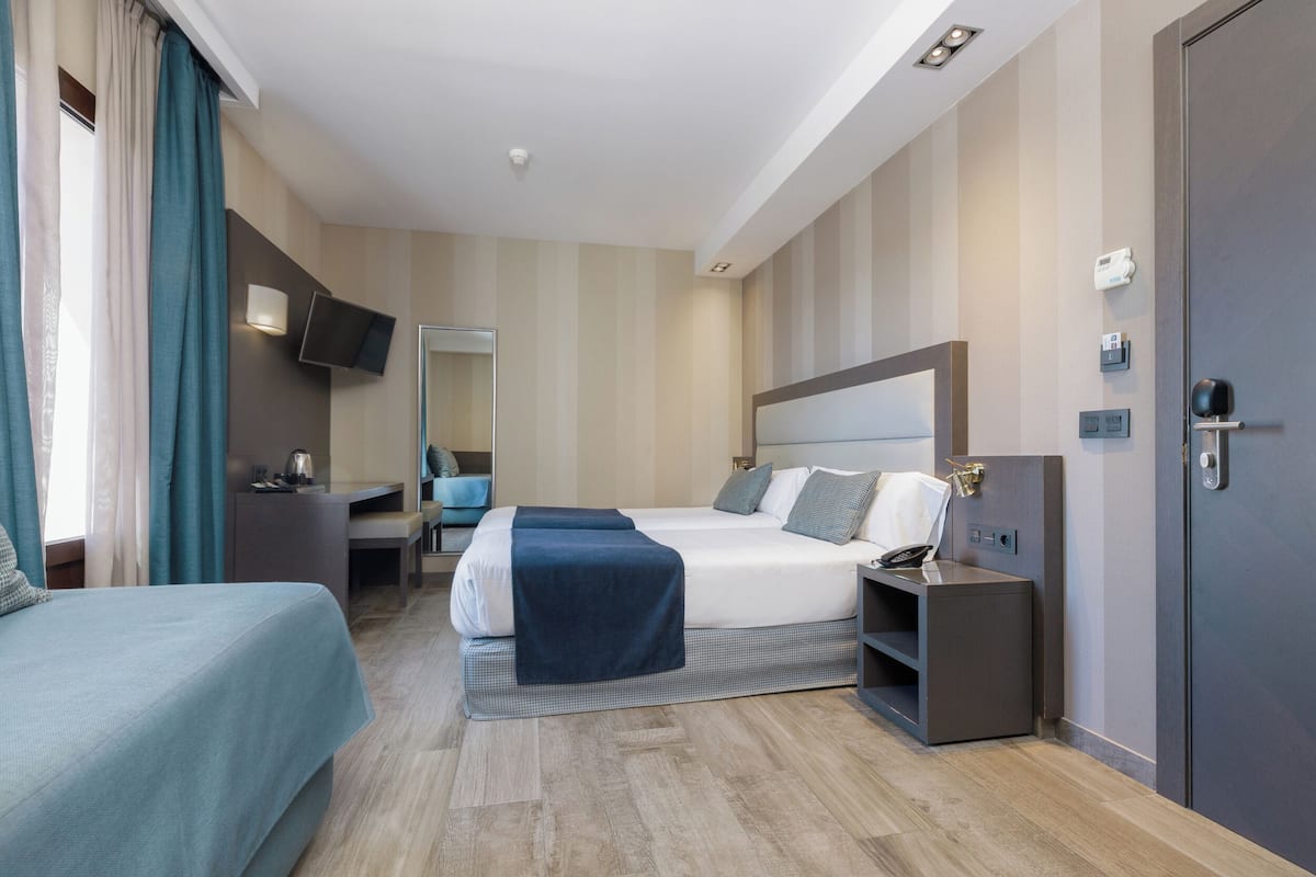 Una habitación de hotel moderna con una cama grande, un escritorio, una silla, un televisor montado en la pared y una puerta con pomo.