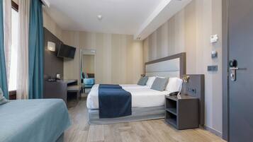 Habitación de hotel con cama, mesita de noche, escritorio, silla y televisor en la pared.