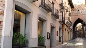 A building with large windows, a stone facade, and a cobblestone street. - Hotel Reina Cristina (Teruel)