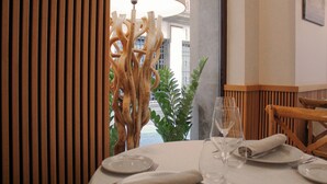 A dining table set with plates, glasses, and a napkin, with a wooden chair and a plant in the background. - Hotel Reina Cristina (Teruel)