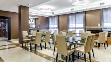 A spacious dining area with multiple tables and chairs, large windows with curtains, and a modern chandelier.
