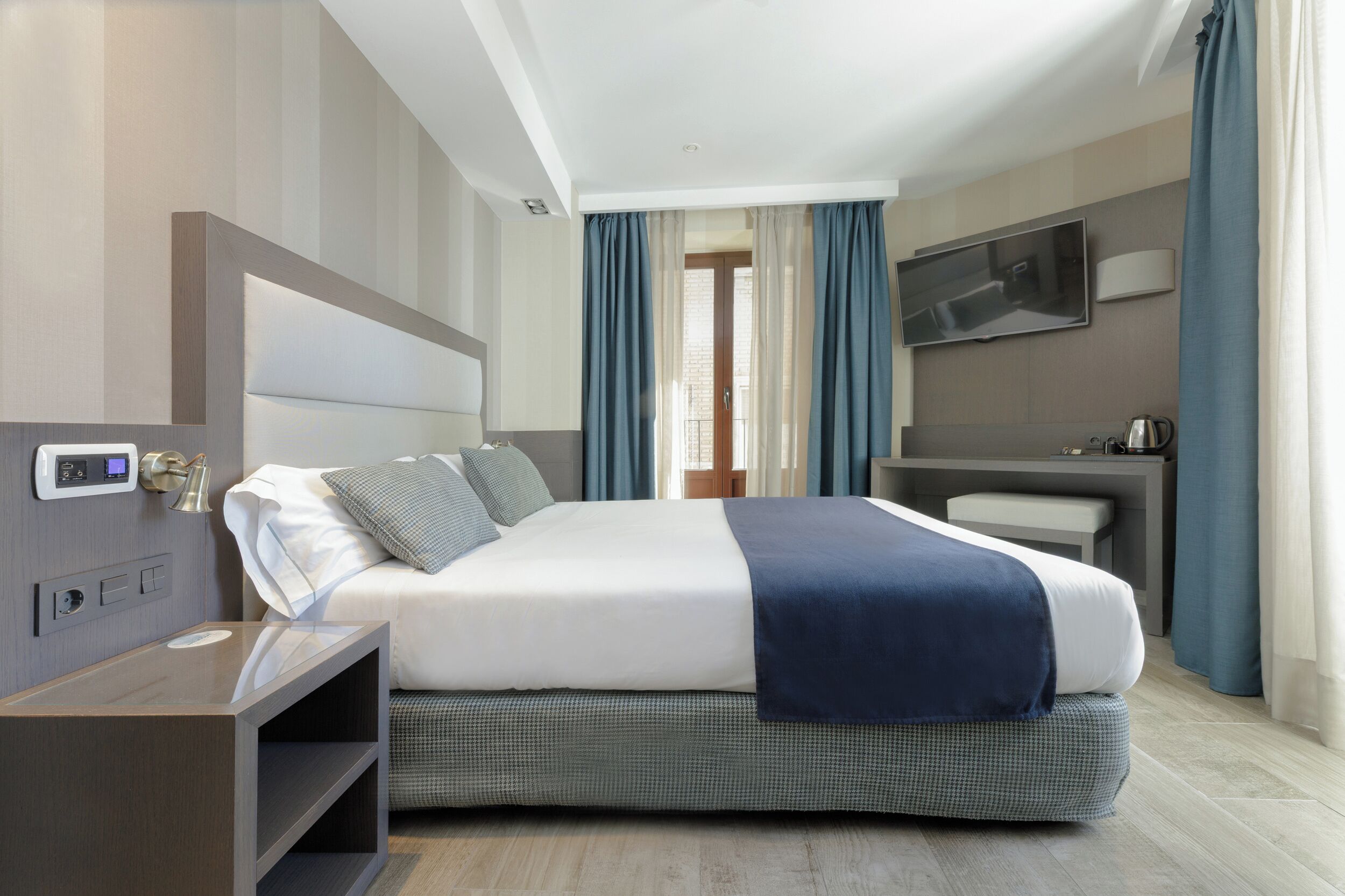 A modern hotel room with a large bed, bedside table, and a flat-screen TV mounted on the wall.