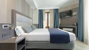 A modern hotel room with a large bed, bedside table, and a flat-screen TV mounted on the wall.
