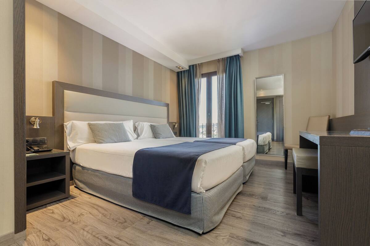 Una habitación de hotel con una cama grande, mesitas de noche, un escritorio y un espejo.