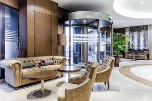 A lobby with a tufted sofa, armchairs, a round table, and a revolving door. - Hotel Reina Cristina (Teruel)