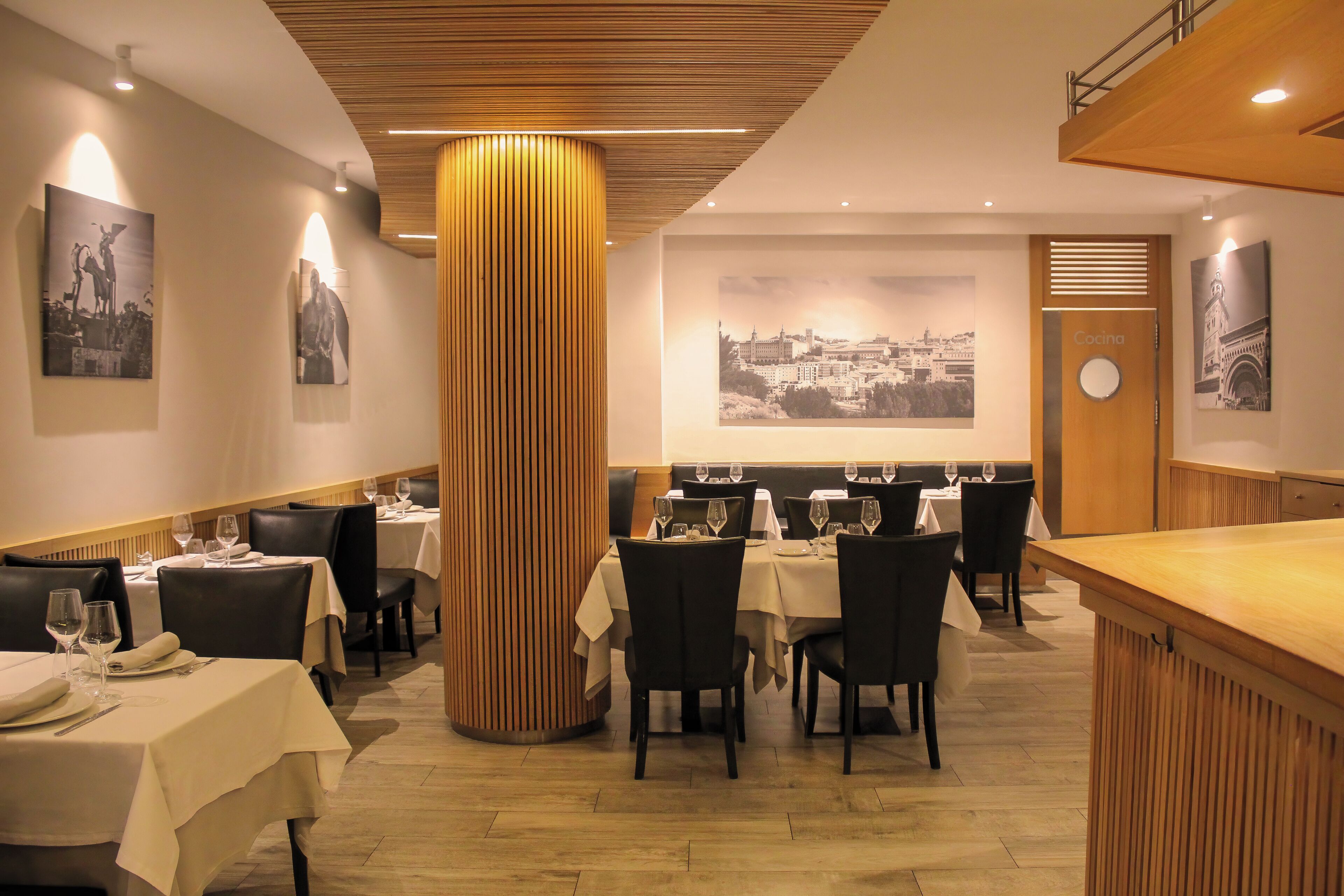 A restaurant with tables set for dining, a wooden column, and framed pictures on the walls.