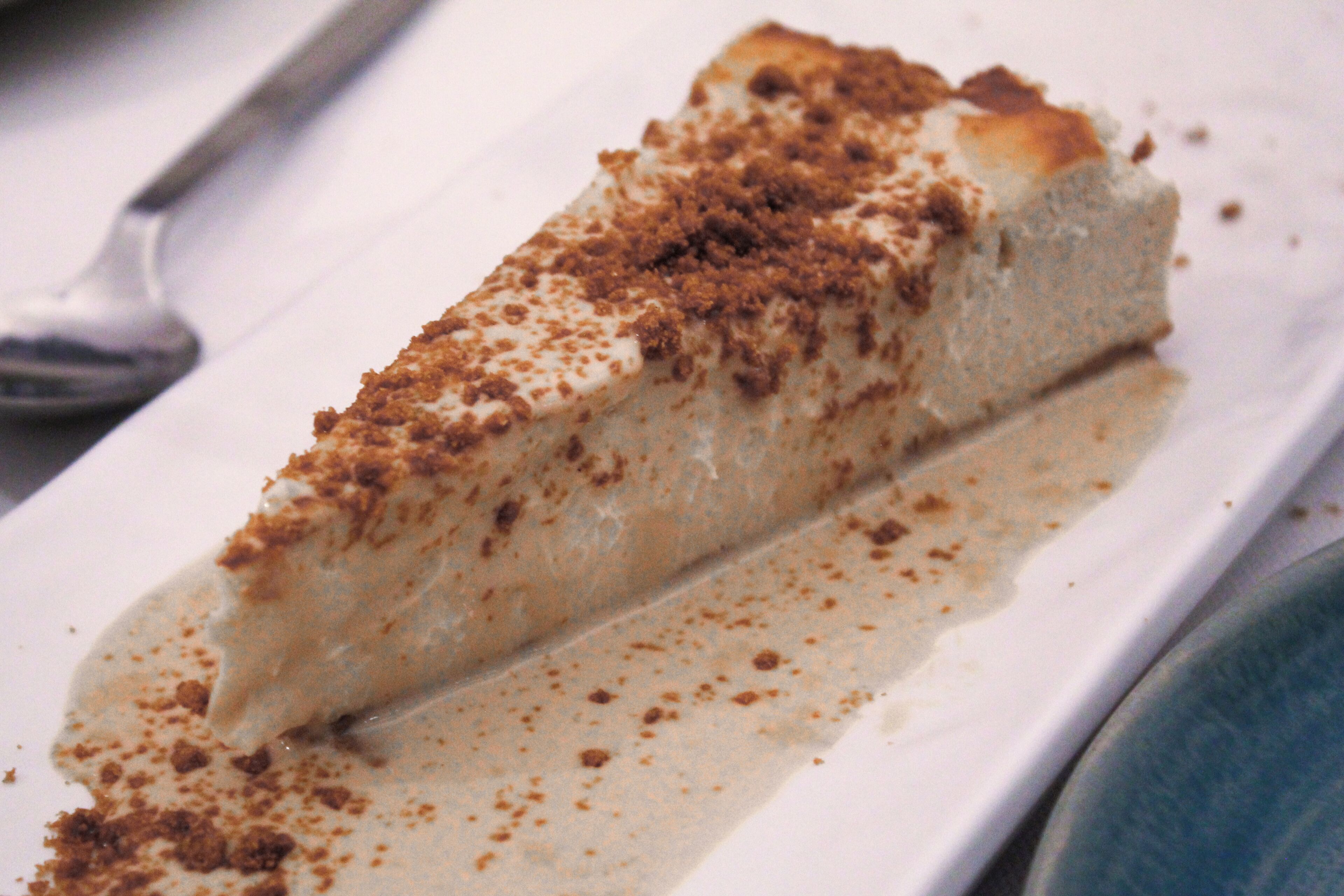Una porción de pastel de queso con cobertura desmenuzable sobre un plato blanco.