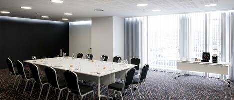 A conference room with a long table, chairs, and a large window with blinds.
