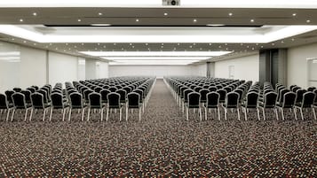 Un salón de conferencias con filas de sillas, una alfombra estampada e iluminación empotrada en el techo.