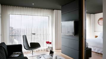Una habitación de hotel moderna con un ventanal grande, un televisor de pantalla plana, una cama y un área de descanso con una mesita de centro.