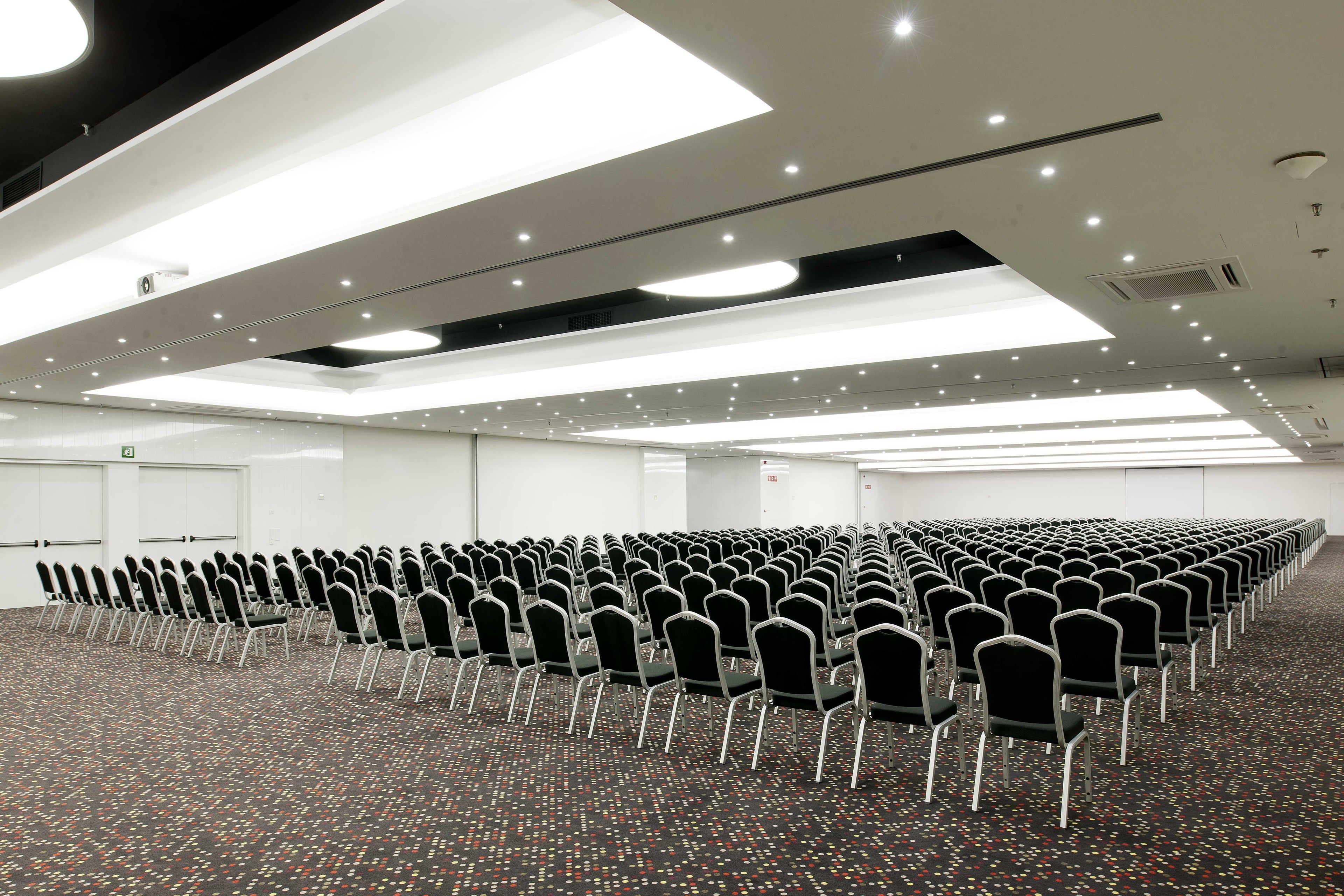 A conference room with rows of chairs, a patterned carpet, and recessed ceiling lighting.