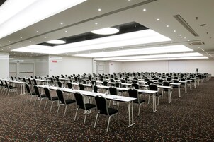 A conference room with rows of tables and chairs, equipped with glassware and a carpeted floor.