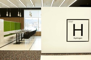 A restaurant with a modern interior, featuring a green partition, white walls, and a large window offering a city view.