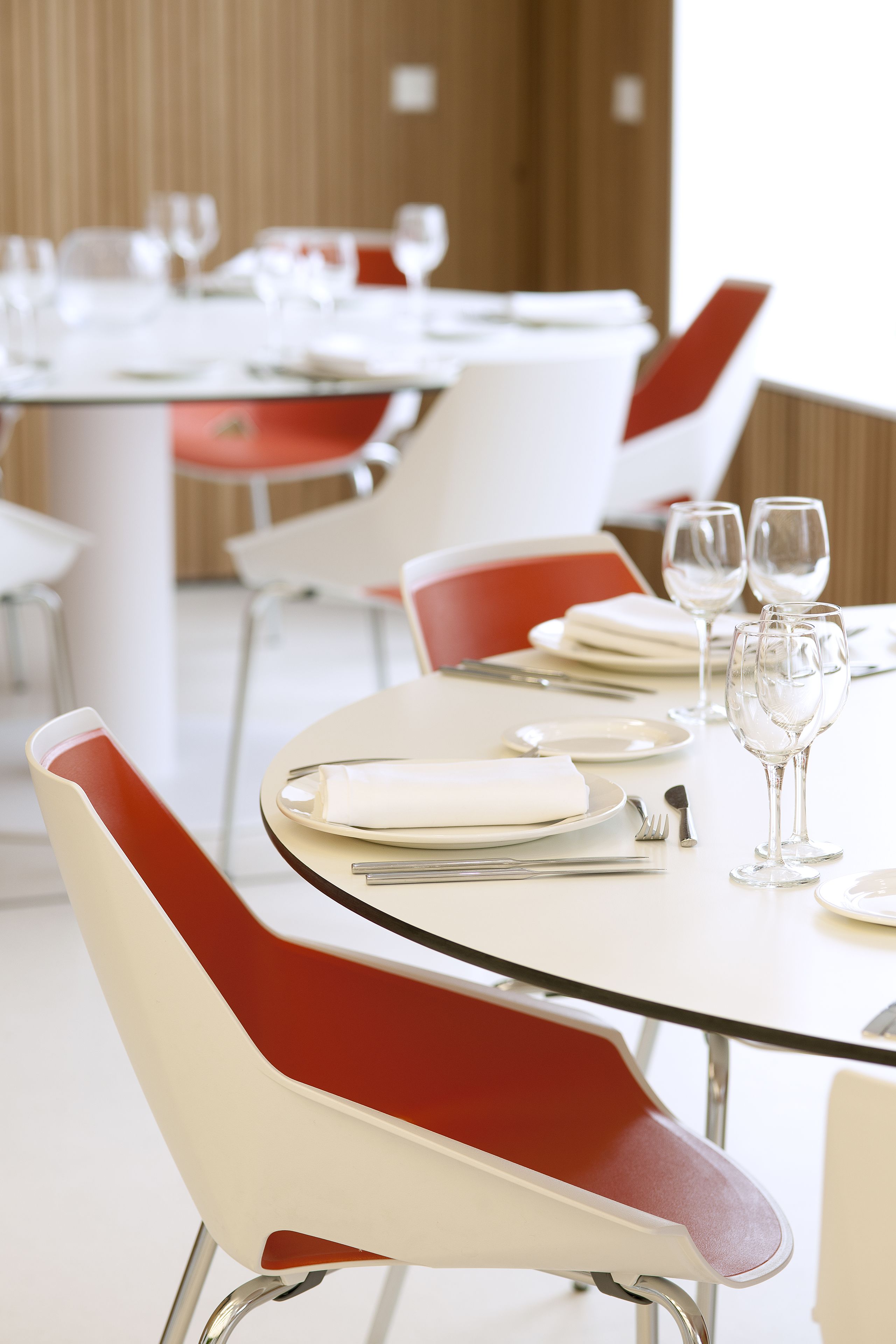 A dining area with tables set for two, featuring modern chairs with red cushions and white tablecloths.