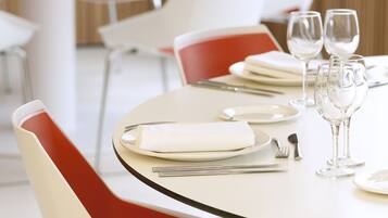 A dining area with tables set for two, featuring modern chairs with red cushions and white tablecloths.
