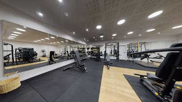 Un gimnasio con diverso equipo de ejercicio, un muro con espejos y suelo de madera.