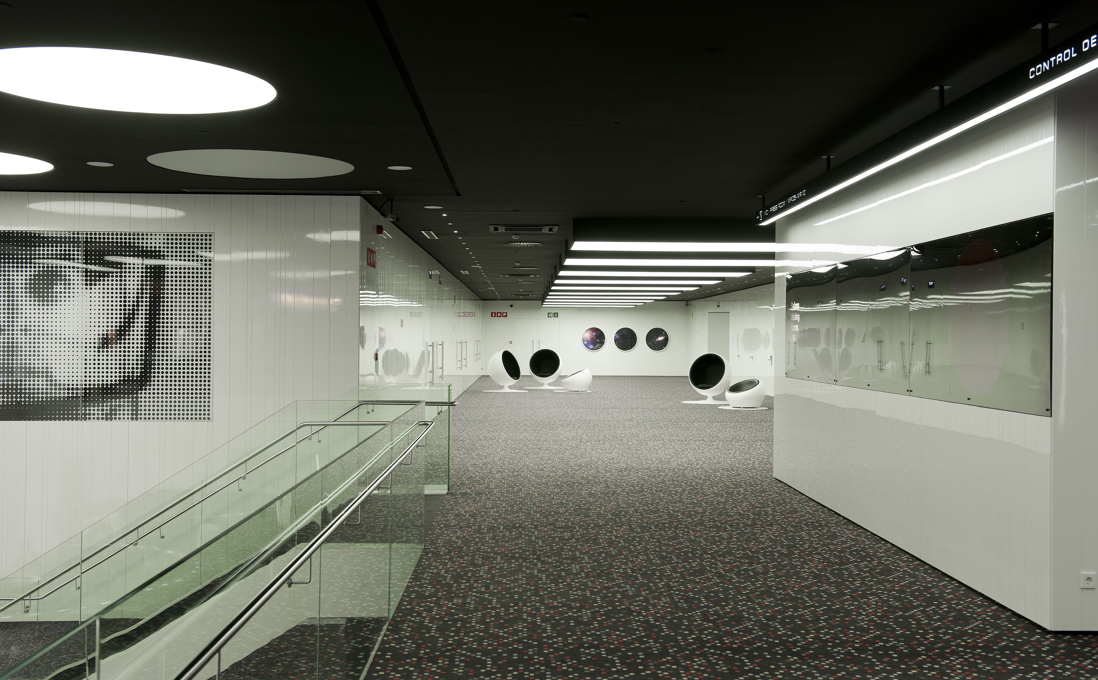 Un interior moderno con una escalera de vidrio, una instalación de arte digital y un panel de control.