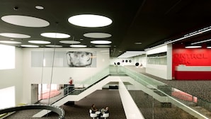 Un interior moderno con una escalera central, barandillas de cristal y una zona de recepción.